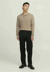 Camisa polo de manga longa bege com colarinho, combinada com calças pretas e sapatos pretos. Design simples com um ajuste relaxado e textura suave.