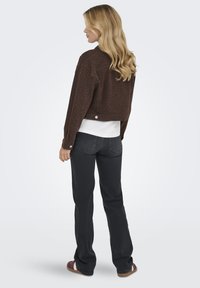 Chaqueta corta de estampado de leopardo marrón hecha de tela suave, con detalles en botones, llevada sobre una blusa blanca y combinada con pantalones de mezclilla negros.