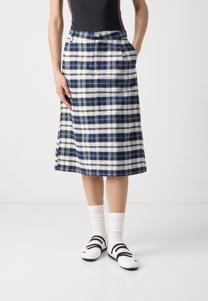 Woman wearing a knee-length blue and white plaid skirt, black top, white socks, and white shoes with black straps.