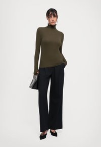 Olive green fitted turtleneck top, long sleeves, paired with high-waisted black wide-leg trousers and black pointed-toe heels.