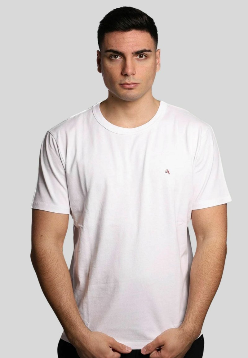 T-shirt bianco in cotone con scollo rotondo, maniche corte e un piccolo logo rosso sul lato sinistro del petto. Texture liscia, vestibilità regolare.