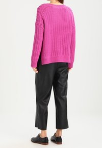 Fuchsia stickad tröja med ett strukturerat mönster, tillsammans med svarta läderbyxor i cropped-modell och svarta snörskor.