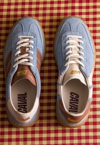 Paire de baskets en daim bleu et marron avec des lacets blancs sur une surface en tissu à carreaux rouges et jaunes.