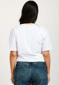 Maglietta bianca corta con maniche corte e scollatura rotonda, abbinata a jeans in denim blu con tasche posteriori e finitura sfumata.