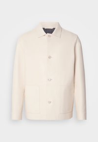 Veste crème boutonnée avec col et deux poches avant, présentée sur un fond clair uni.