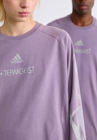 Sweat-shirt purple à col rond en coton, ornée d'un motif graphique discret sur la manche et du logo adidas sur le devant.