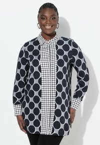 Chemise à boutons noire et blanche avec de grands pois et un motif rayé. Elle dispose de manches longues et d'un col.