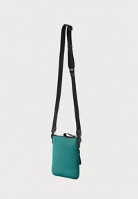 Tyrkysová kabelka cez rameno vyrobená z hladkého materiálu. Má čierny popruh s textom, zapínanie na zips a zaoblené rohy.