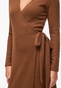 Robe portefeuille côtelée marron avec manches longues, encolure en V, et détail à nouer à la taille. Texture lisse avec une silhouette ajustée.