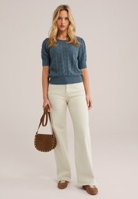 Maglione blu a maniche corte lavorato a maglia con un motivo testurizzato, abbinato a pantaloni beige chiaro a zampa d'elefante e una borsa a tracolla in suede marrone.