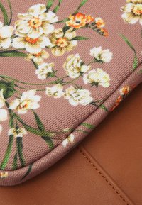 Textil con patrón floral en beige y naranja sobre un fondo rosa, con una base de cuero marrón y un borde de tela texturizada.