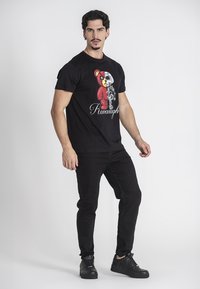 Camiseta negra con un gráfico colorido de un oso con detalles, combinada con jeans negros y zapatillas oscuras. Diseño simple y casual.