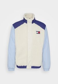 Giacca in pile con corpo crema, maniche blu e navy, chiusura con bottoni a pressione e patch con logo sul petto. Presenta polsini e orlo elastici.
