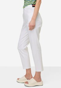 Pantalons blancs à jambes droites avec poches latérales, en tissu léger. Associés à des sandales à plateforme beiges, dotées d'une texture lisse.