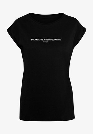 Schwarzes T-Shirt mit lockerer Passform und aufgerollten Ärmeln. Mit weißem Text: "JEDER TAG IST EIN NEUER ANFANG" und "#hoffnung" auf der Brust.