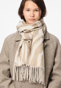 Beige tørklæde med hvide zebra-striber, lavet af et blødt stof. Har frynsekant og en glat tekstur, båret over en grå frakke.