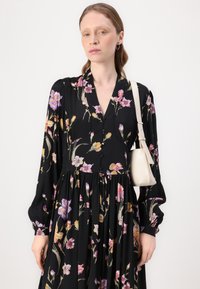 Abito nero a fiori con maniche lunghe, scollatura a V e gonna arricchita. Presenta vivaci motivi floreali e bottoni sul davanti.