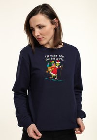 Felpa blu navy con un design grafico giocoso che raffigura il Grinch che scia e regali delle festività. Realizzata in un morbido tessuto testurizzato.