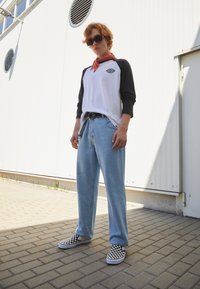 White and black long-sleeve shirt, light denim jeans, black and white checkered slip-on shoes, red bandana tied around neck.