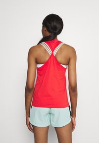 Top deportivo rojo sin mangas con diseño en la espalda cruzada, con tirantes blancos. Combinado con pantalones cortos de color menta claro, que muestran un ajuste relajado.