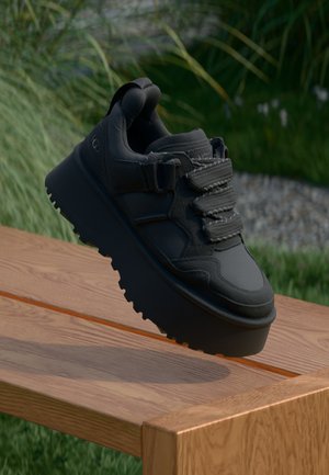 Black sneaker featuring a textured leather upper, three black lace loops, thick black platform sole with tread, and pull tab at the heel.