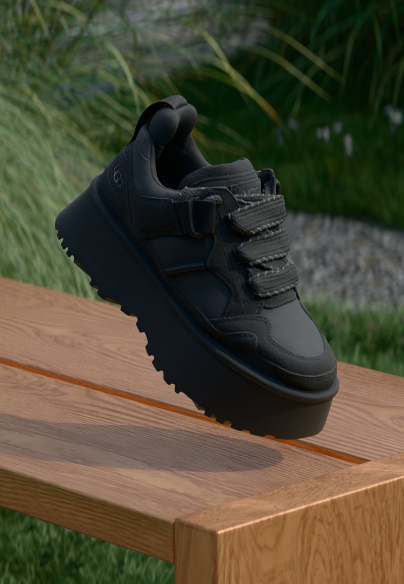 Svart sneaker med en teksturert læroverdel, tre svarte snørehull, tykk svart platåsåle med mønster, og en hentetab i hælen.