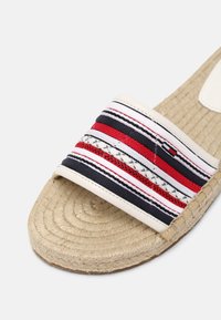 Sandale espadrille avec semelle tissée beige et bride en tissu présentant des rayures horizontales rouges, blanches et bleu marine avec des détails cousus.