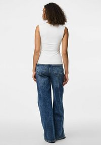 Top sin mangas blanco combinado con jeans de denim azul de pierna ancha. El conjunto presenta un diseño ajustado con una textura suave y costuras mínimas.