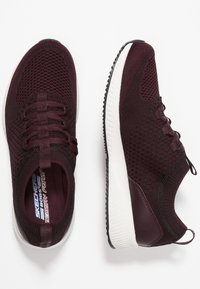 Vinröda stickade sneakers med snörning, vit mellansula, texturerat tyg och dragflikar vid hälen för enkel påtagning.