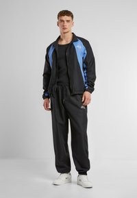 Trackjakke i sort med blå accenter, med lynlåslukning og elastiske manchetter, parret med matchende sorte sweatpants og hvide sneakers.