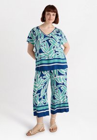 Blumiges Loungewear-Set bestehend aus einem V-Ausschnitt-Oberteil und weiten Hosen in Blau, Grün und Weiß; der Stoff hat eine glatte, leichte Textur.