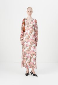 Bloemen maxi-jurk met lange doorschijnende mouwen; heeft roze en bruine bloemenpatronen op een witte achtergrond. Gecombineerd met zwarte schoenen met hakken en een bruine tas.