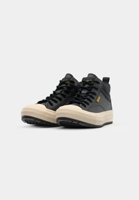 Baskets montantes en cuir noir avec semelles en caoutchouc beige, présentant un motif texturé, des lacets noirs et une languette à l'arrière.