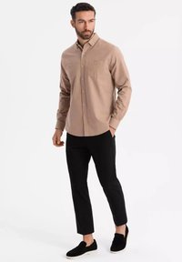 Chemise boutonnée marron clair avec deux poches poitrine, associée à un pantalon noir ajusté et des chaussures noires à enfiler. Tissu lisse au design classique.