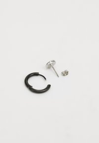 Black hoop earring with a smooth, curved design, accompanied by a silver stud earring with a round shape and a silver backing near it.