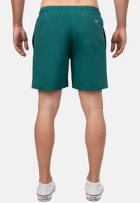 Pantaloni da bagno verdi da uomo con vita elastica e tasche laterali. Presentano una tasca posteriore con pattina. Tessuto liscio e leggero.