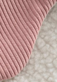 Tessuto rosa texturizzato con un motivo a righe verticali su un lato, in contrasto con una base beige morbida e pelosa dall'altro lato.