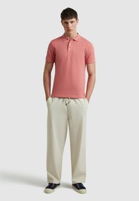 Roze polo shirt met korte mouwen en drie knopen, gecombineerd met crèmekleurige brede broek en marineblauwe sneakers. Soepele stoftextuur met subtiele patronen.