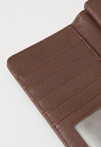 Portefeuille brun texturé avec plusieurs emplacements pour cartes et une section transparente pour l'identification. Présente des lignes diagonales et des bords cousus.