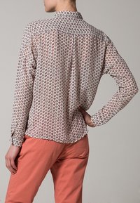 Camicia leggera a maniche lunghe con un motivo rosa e bianco di piccole forme, presenta un colletto con bottoni e polsini abbottonati.