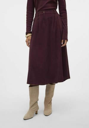 Femme portant une jupe midi taille haute violet foncé, un haut à manches longues assorti, des bottes beiges à talons souples et deux bracelets à un poignet.