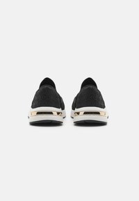 Des chaussures de sport noires avec un motif texturé, présentant un accent doré au niveau du talon et une semelle blanche. Tige lisse avec une entrée élastique.