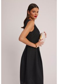 Czarna sukienka bez rękawów z teksturowanymi pasami, dopasowaną górą i rozkloszowanym dołem. Uzupełniona torebką z złotymi akcentami i bransoletką.