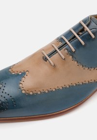 Scarpa in pelle blu e beige con design wingtip, dettagli perforati e lacci beige chiaro su una finitura liscia e lucida.