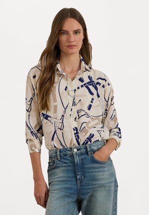 Knapplang skjorte med en tan bakgrunn og et marineblått geometrisk mønster, med krage og oppbrettede ermer, parret med blå denimjeans.