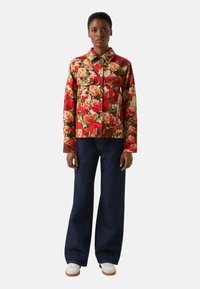 Kurtka w kwiatowy wzór w odcieniach czerwieni i zieleni, zestawiona z szerokimi ciemnymi jeansami i białymi trampkami. Kurtka posiada zapięcie na guziki na przodzie oraz kołnierz.