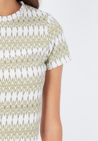 Camisa blanca de manga corta con un patrón de diamantes en amarillo y negro. Textura suave con escote redondo y diseño ajustado.