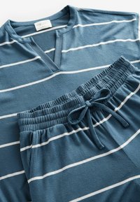 Blauwe gestreepte lounge-outfit gemaakt van zachte stof. Bevat een shirt met korte mouwen en een halve knoopsluiting, evenals bijpassende broek met elastische taille en trekkoord.