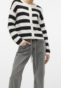 Svart och vitrandig stickad cardigan med rund nacke, texturerat tyg och stora knappar. Kombinerad med grå, löst sittande byxor.