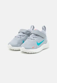 Sive patike za sport s gornjim dijelom od mrežaste tkanine i bijelim đonom. Značajke uključuju plavi Swoosh logo, narančaste detalje i čičak trakicu za zatvaranje.